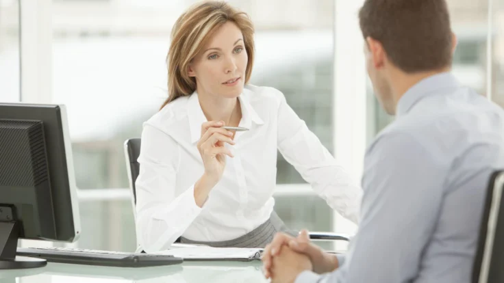 Recruteuse qui interroge un candidat assis en face d'elle pendant un entretien d'embauche