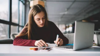 Candidat qui prend des notes et surligne des informations à la main devant son ordinateur