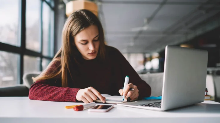 Candidat qui prend des notes et surligne des informations à la main devant son ordinateur