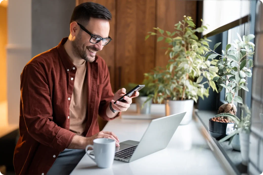Homme souriant travaillant sur son CV en ligne avec son ordinateur portable et son téléphone